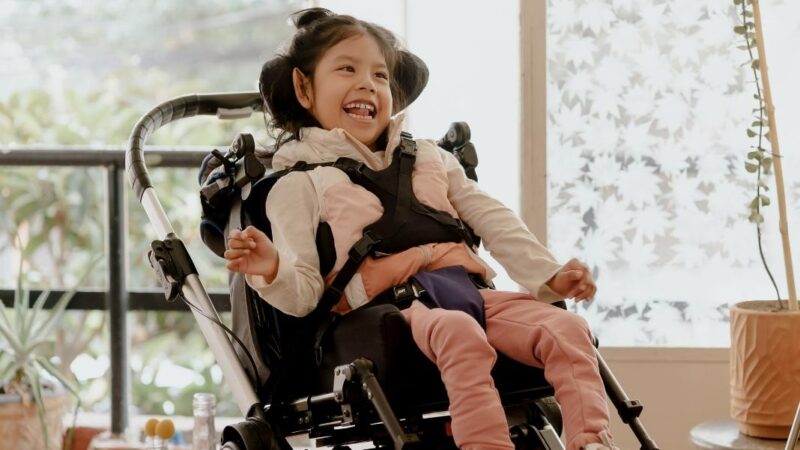 Niña con discapacidad sonriendo y sentada en un coche