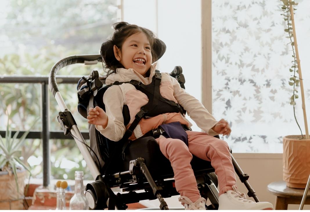 Niña con discapacidad sonriendo y sentada en un coche