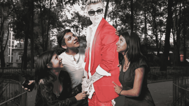 Dos mujeres y un hombre junto a una figura de cartón de Justin Bieber