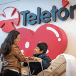 Madre e hijo con discapacidad y atrás logo de la Teletón