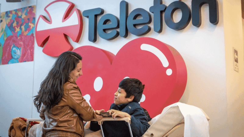 Madre e hijo con discapacidad y atrás logo de la Teletón