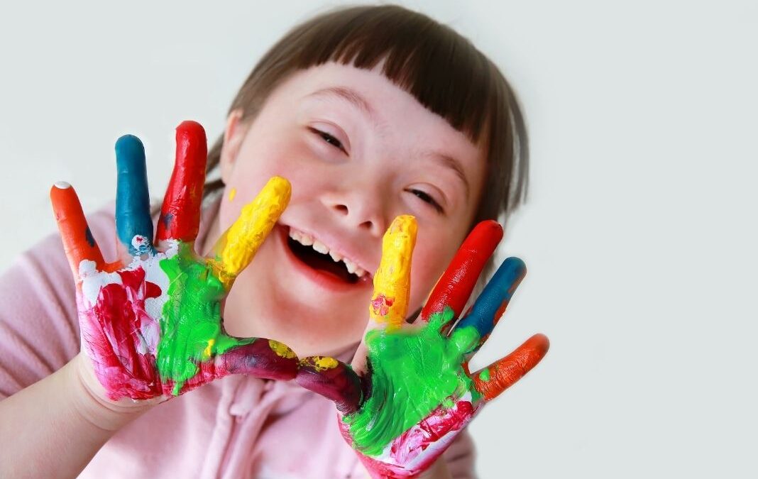niña con síndrome de down mostrando manos pintadas
