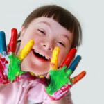 niña con síndrome de down mostrando manos pintadas