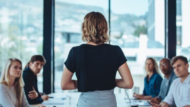 Mujer de espalda frente a mesa con diversas personas