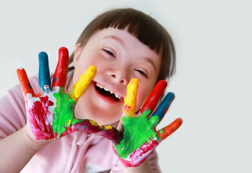 niña con síndrome de down mostrando manos pintadas