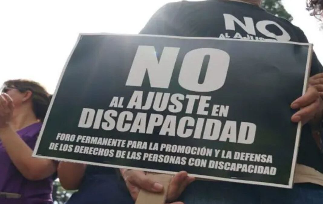 Persona sujetando un afiche de "No al ajuste en discapacidad"