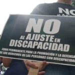 Persona sujetando un afiche de "No al ajuste en discapacidad"