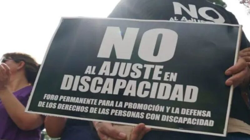 Persona sujetando un afiche de "No al ajuste en discapacidad"