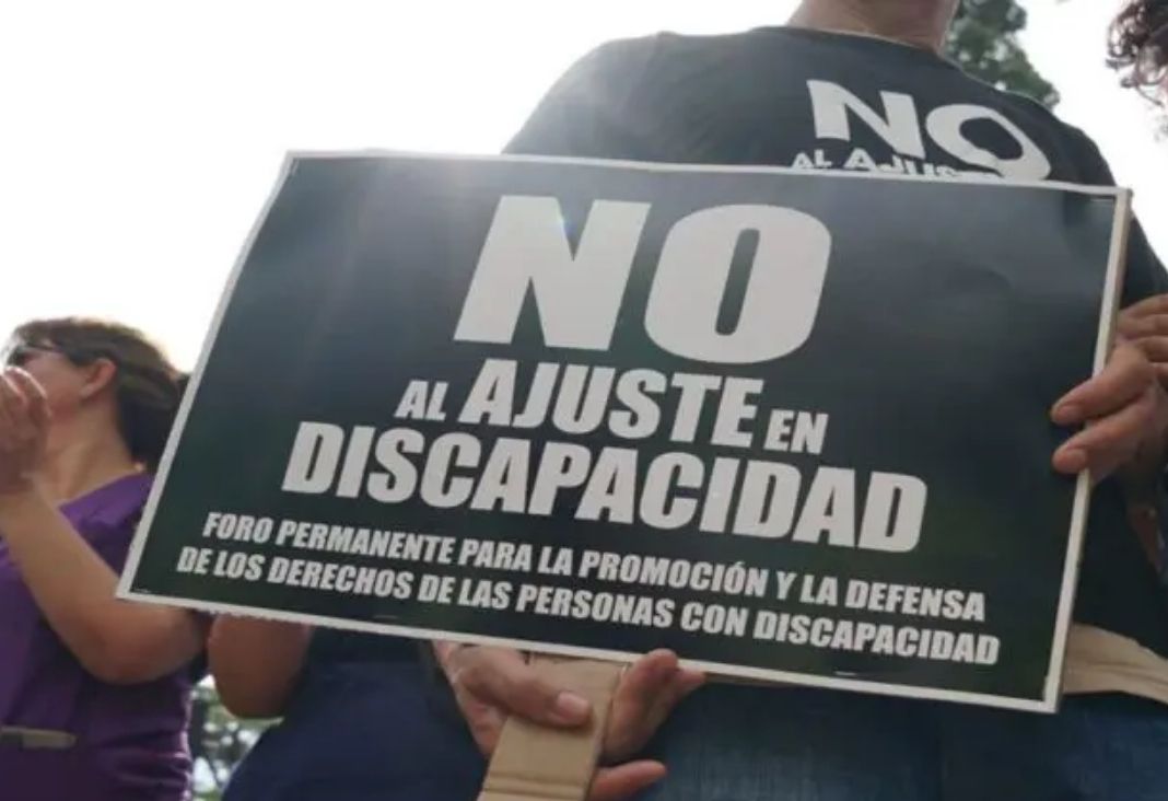 Persona sujetando un afiche de "No al ajuste en discapacidad"
