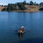 Mujer pescando arriba de un bote y detrás el paisaje de un lago