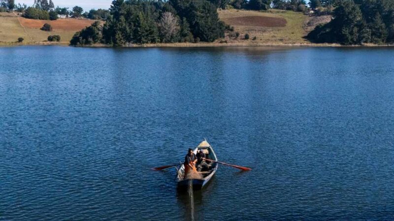 Mujer pescando arriba de un bote y detrás el paisaje de un lago