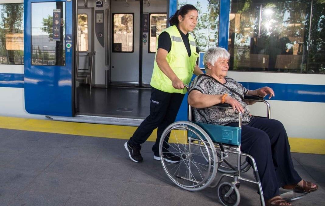 asistente de empresa efe llevando a mujer mayor en silla de ruedas y de fondo un tren