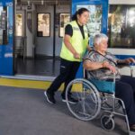 asistente de empresa efe llevando a mujer mayor en silla de ruedas y de fondo un tren