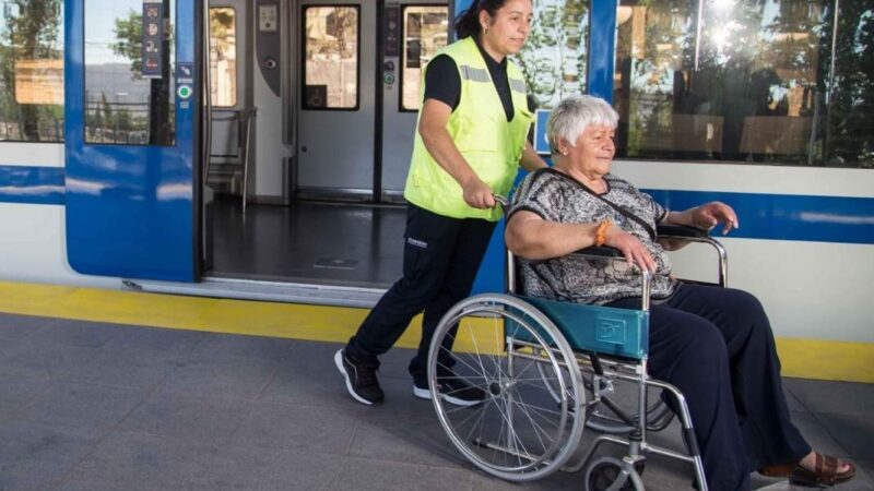 asistente de empresa efe llevando a mujer mayor en silla de ruedas y de fondo un tren
