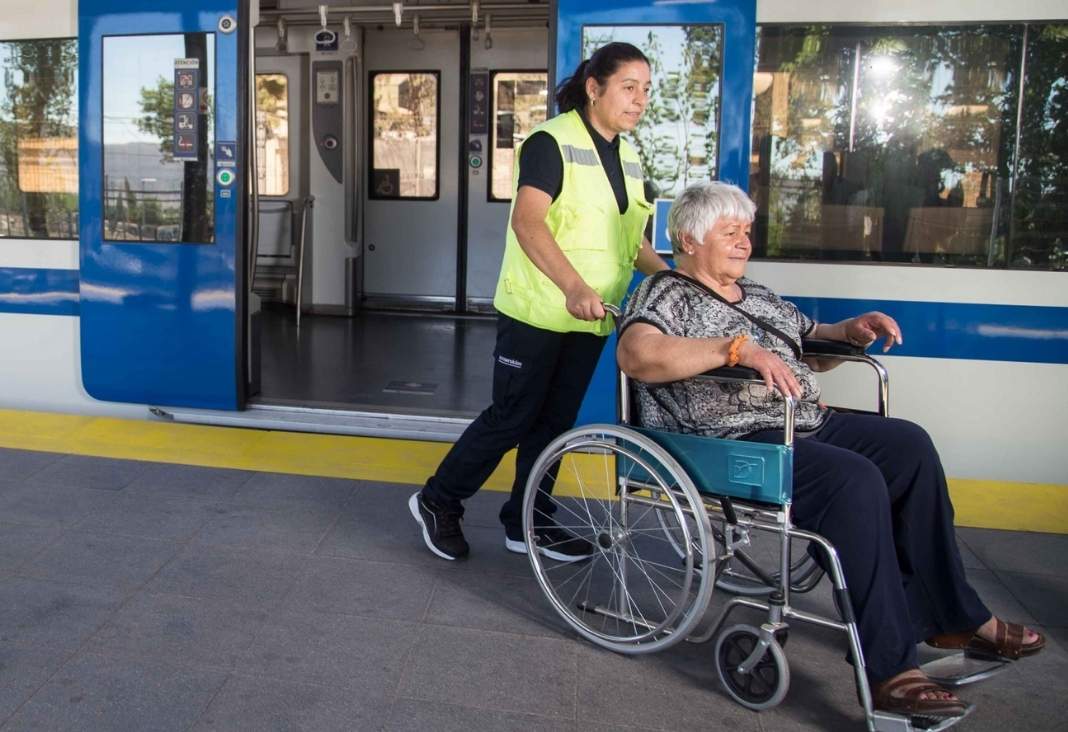 asistente de empresa efe llevando a mujer mayor en silla de ruedas y de fondo un tren