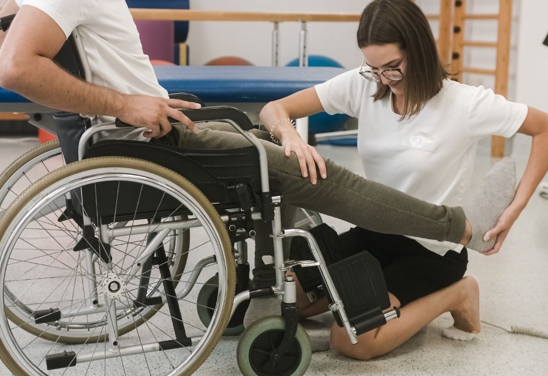 Mujer haciendo rehabilitación a persona en silla de ruedas